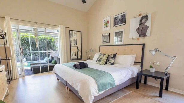 A bedroom with a bed, bedside table, lamp, and artwork on the wall. - Poolside Palms Getaway- Near Tampa Brandon Valrico (Valrico)