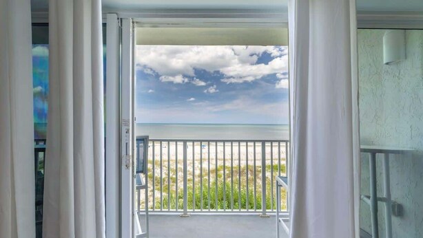 Une vue depuis un balcon doté d’une rambarde en métal, avec un ciel dégagé et une plage lointaine.