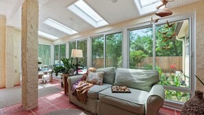 Een zonnige kamer met een bank, een lamp en uitzicht op groen.