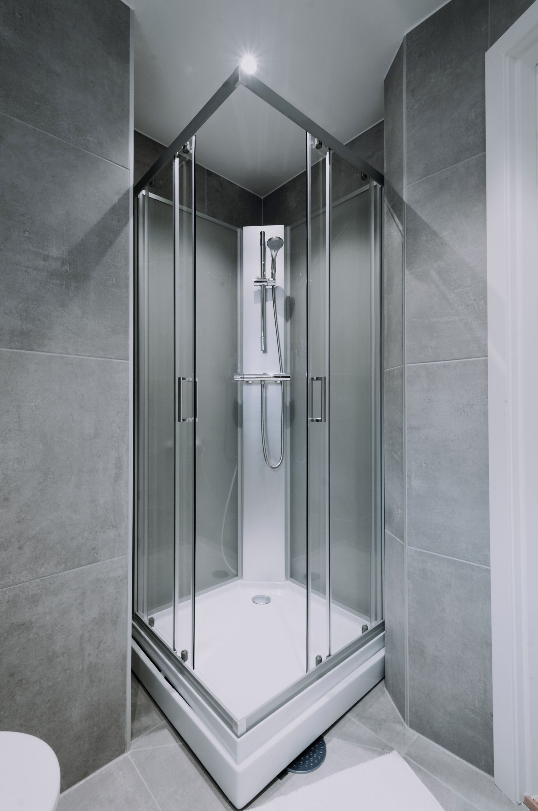 A modern shower enclosure with a glass door, a handheld showerhead, and a built-in seat.