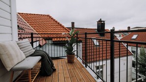 Una terrassa de fusta amb una banca i una planta en test, amb vista a un barri amb teulades vermelles.