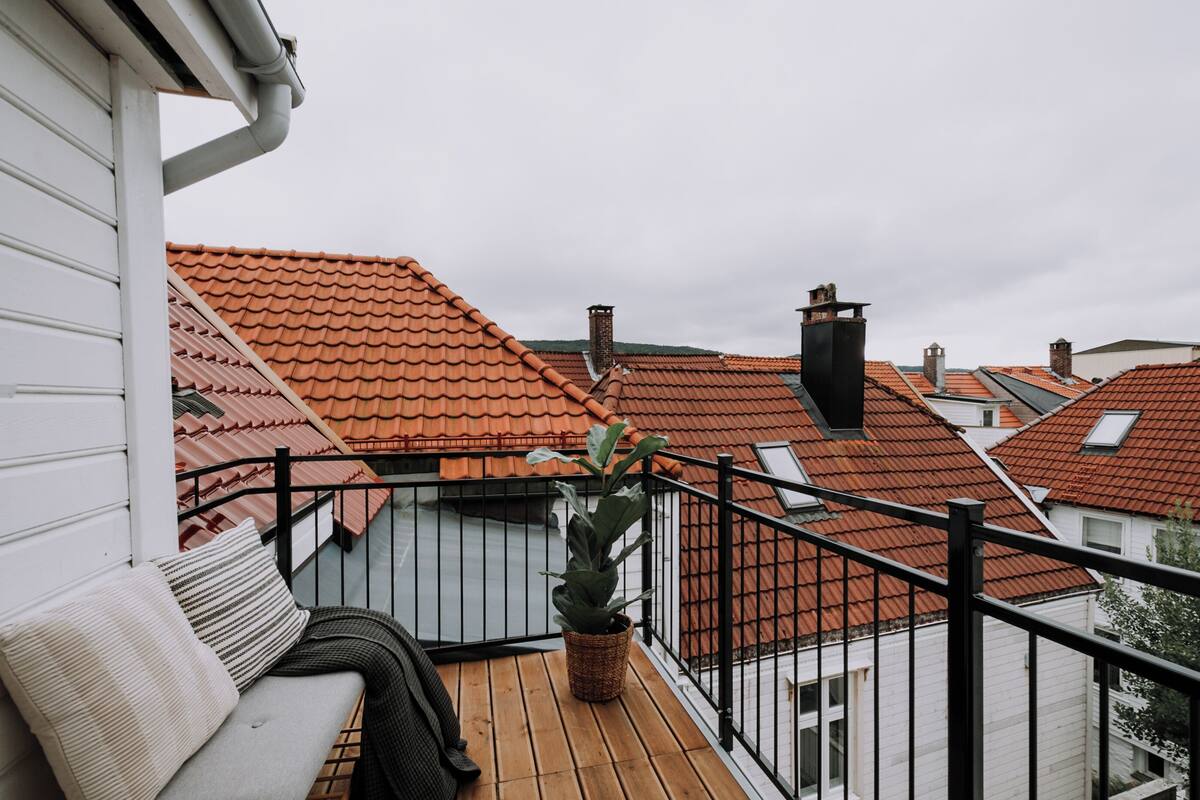 A balcony with a wooden floor, a black metal railing, and a potted plant.