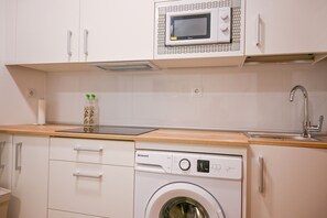 Une cuisine compacte équipée d’un lave-linge intégré, d’un four à micro-ondes et d’un évier.