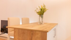 A wooden table with a glass vase containing white flowers and green foliage.