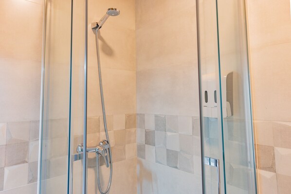 A glass-enclosed shower with a handheld showerhead and a wall-mounted faucet.