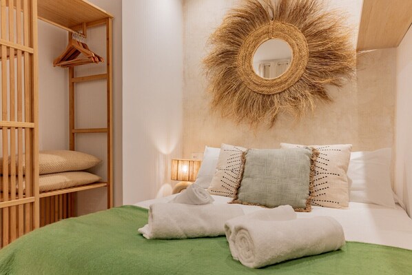 Un dormitorio ordenado con cama, almohadas, un espejo colgado y un armario de madera.