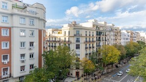 Un edificio residencial de varios pisos con balcones, una calle peatonal y árboles.