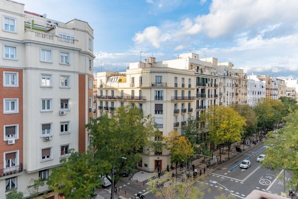 Un edificio residencial de varios pisos con balcones, una calle peatonal y árboles.