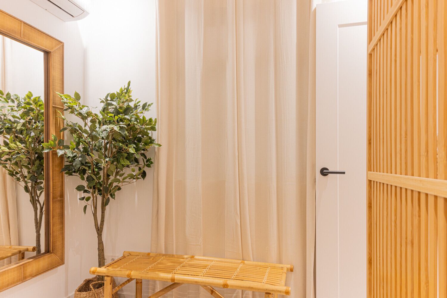 Un baño con puerta de madera, un espejo y una pequeña mesa con una planta.