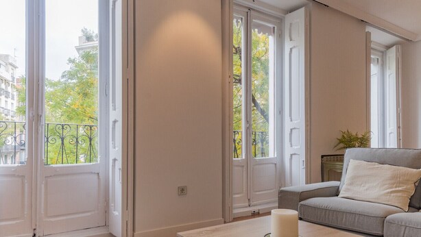 Amplia habitación con ventanas grandes, un sofá gris y una mesa con una vela.
