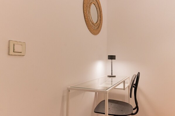 Una habitación minimalista con una mesa de vidrio, una silla negra, un tapiz tejido y un interruptor de luz.