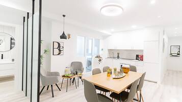 Une cuisine moderne avec des meubles blancs, un coin repas avec une table et des chaises en bois, et un espace de vie avec un canapé et une table basse.