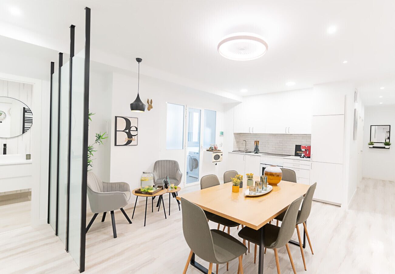A modern kitchen with white cabinets, a dining area with a wooden table and chairs, and a living space with a sofa and a coffee table.
