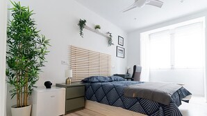 A modern bedroom with a bed, bedside tables, a small white cabinet, a potted plant, and a window with blinds. - London: room with comfort, convenience and shared areas Chamartín - Mauricio Legendre (Madrid)