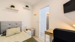 A bedroom with a bed, bedside table, lamp, and a TV mounted on the wall.