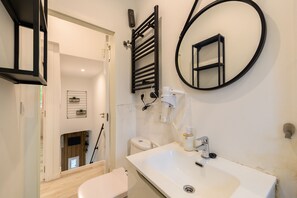 Ein modernes Badezimmer mit einem weißen Waschbecken, einem schwarzen Handtuchhalter, einem runden Spiegel und einer Toilette.