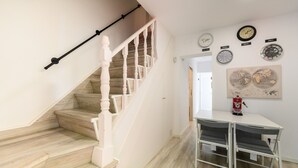 A staircase with wooden steps and white railings, a small table with chairs, and several clocks on the wall.