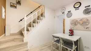 Una escalera con barandillas blancas, una mesa de comedor con dos sillas, relojes de pared y mapas.