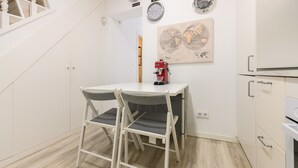 Una pequeña cocina con una mesa blanca y dos sillas, una cafetera y un mapa del mundo en la pared.