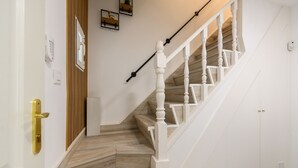 Een trap met houten treden en witte leuningen, een deur met een messing knop, en een lichtschakelaar op de muur.