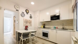 Een moderne keuken met witte kastjes, een magnetron, een oven en een spoelbak. Er staat een eettafel met stoelen.