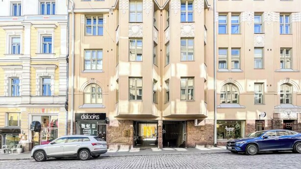 A building with a central entrance, two parked cars, and a cobblestone street. - 5 Room Apartment by the Esplanade Park (Helsinki)