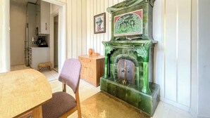 A room with a wooden dining table, a green fireplace with a decorative panel, a wooden cabinet, and a framed picture on the wall. - 5 Room Apartment by the Esplanade Park (Helsinki)