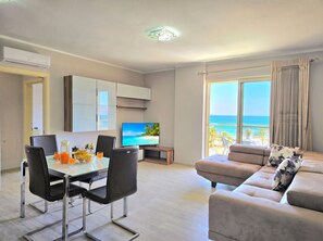 Ein modernes Wohnzimmer mit Essbereich, einem Flachbildfernseher und einem großen Fenster mit Meerblick.