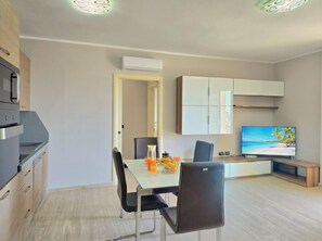 A modern kitchen with built-in appliances, a dining area with a table and chairs, and a TV displaying a beach scene.