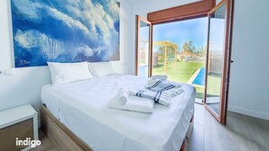A bedroom with a large bed, white bedding, and a view of a backyard through a sliding glass door.