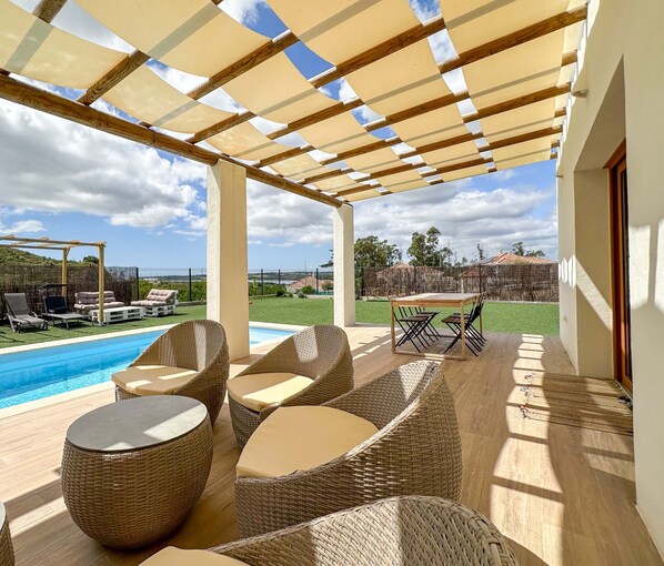 A covered outdoor area with a pool, wicker furniture, and a table with chairs. - Modern Villa • Private Pool • River Views • POV01 (Ayamonte)