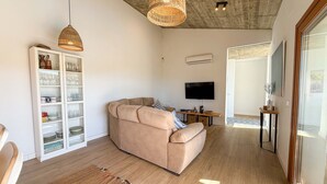 A modern living room with a beige sofa, a television, and a glass cabinet filled with glassware.