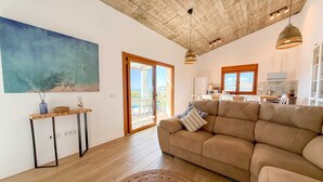 A spacious living area with a large sofa, a painting, a wooden table, and a kitchen in the background.