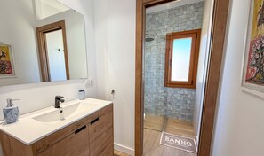 A bathroom with a white sink, wooden vanity, a mirror, and a shower with a brick wall. - Modern Villa • Private Pool • River Views • POV01 (Ayamonte)