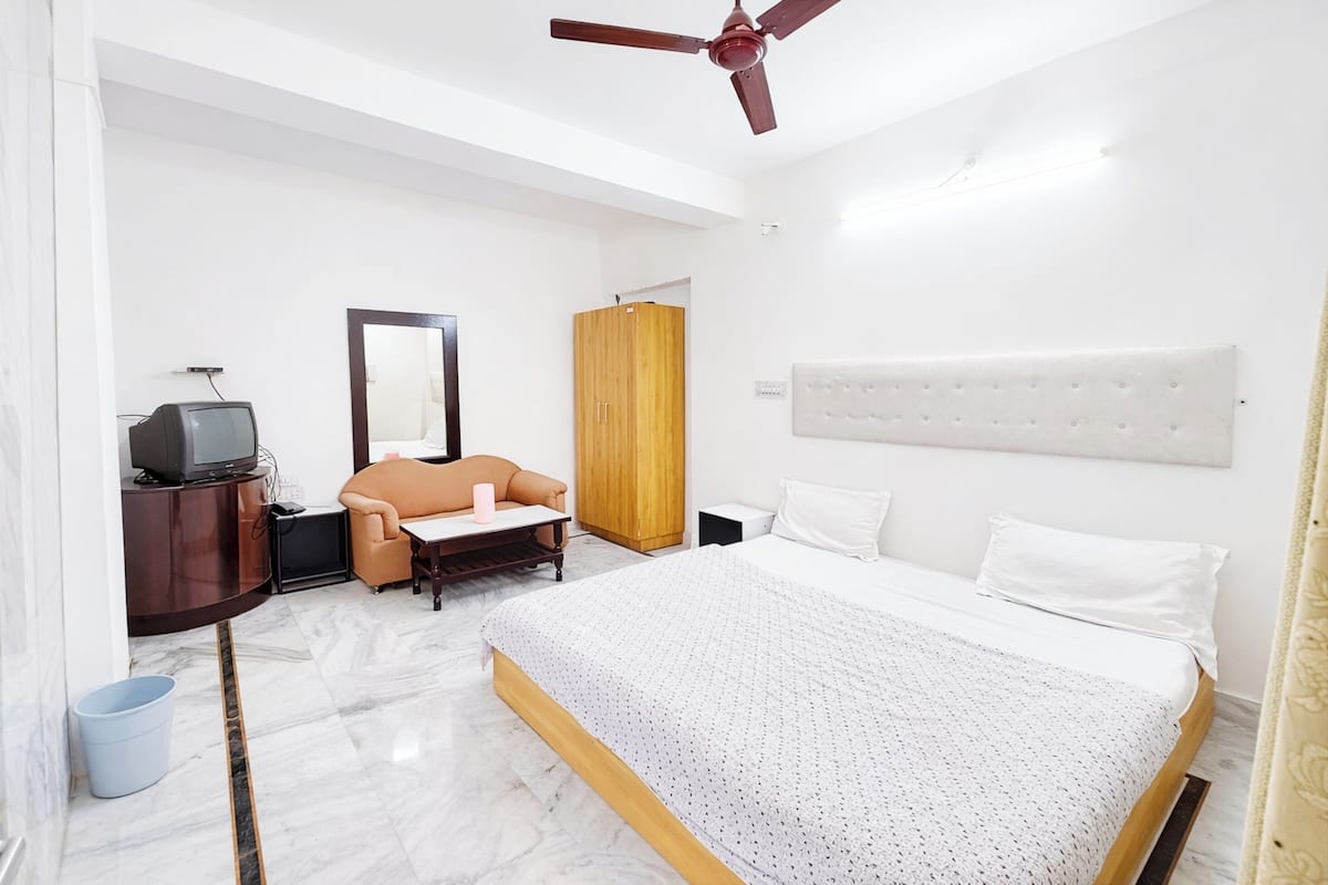 A hotel room with a bed, a television, a wardrobe, a chair, and a ceiling fan.
