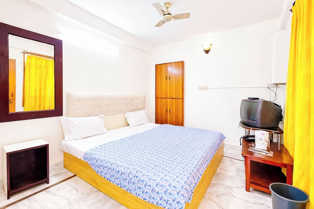 A bedroom with a bed, a wardrobe, a television on a stand, and a ceiling fan.