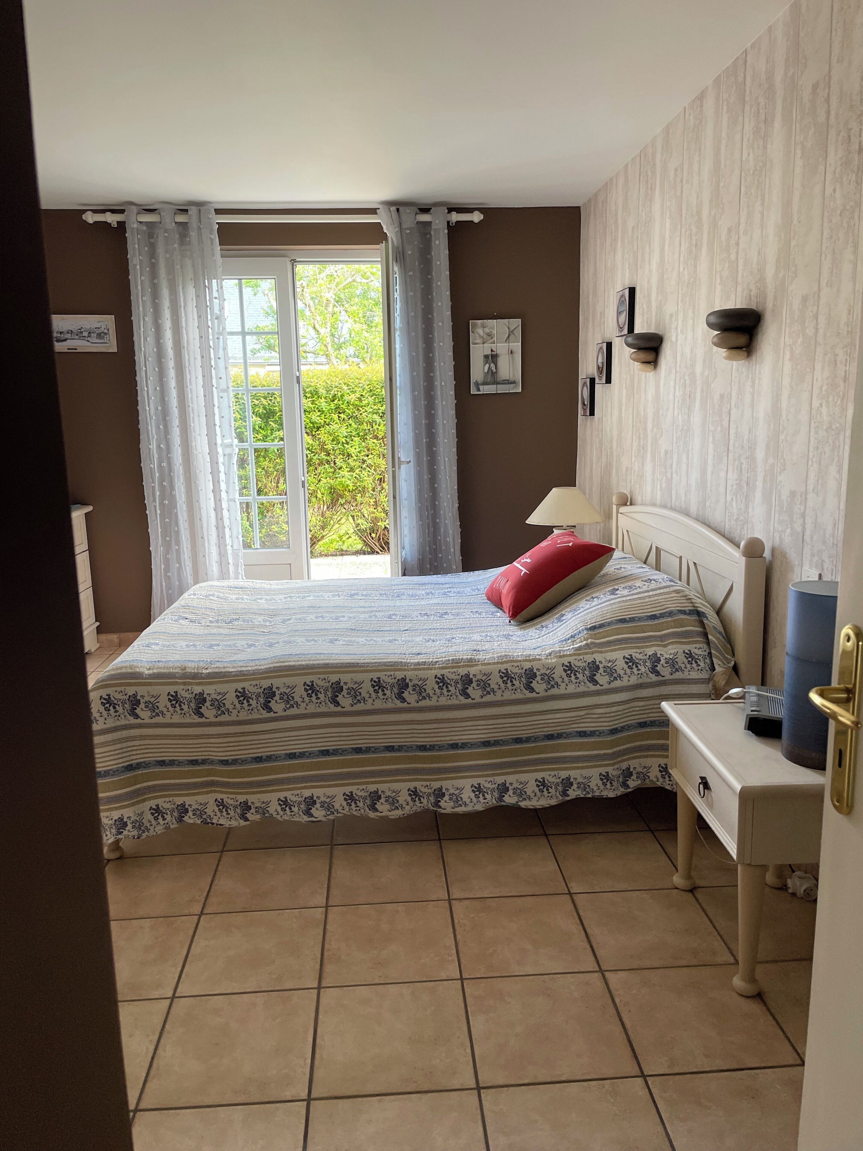 Un dormitorio con una cama, una mesita de noche, una ventana con cortinas y una lámpara de pared.