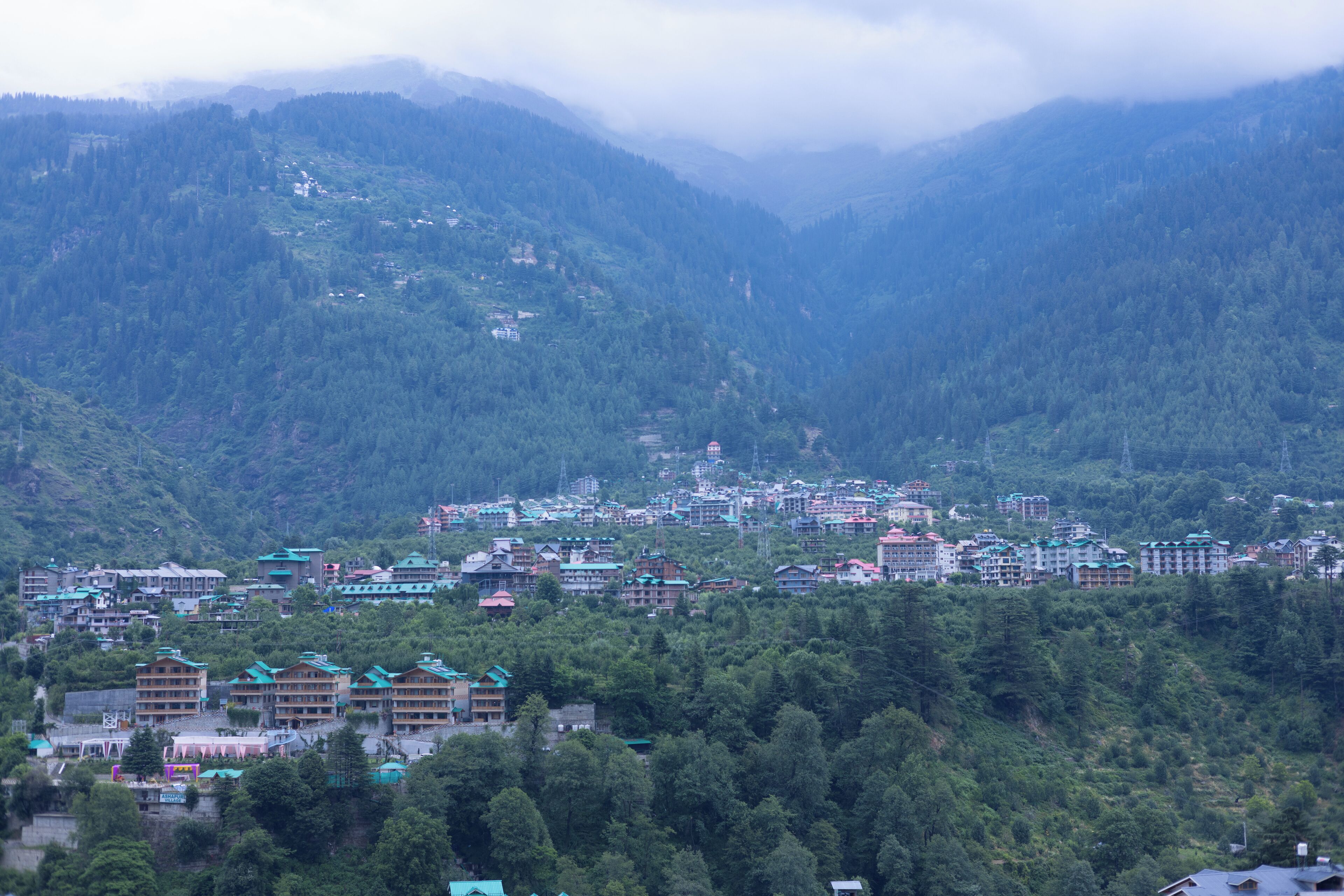 A mountainous town with multiple buildings, including hotels with green roofs, nestled among dense forests.