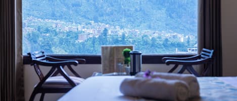 A hotel room with a bed, two chairs, a small table, and a window offering a view of a mountainous landscape.