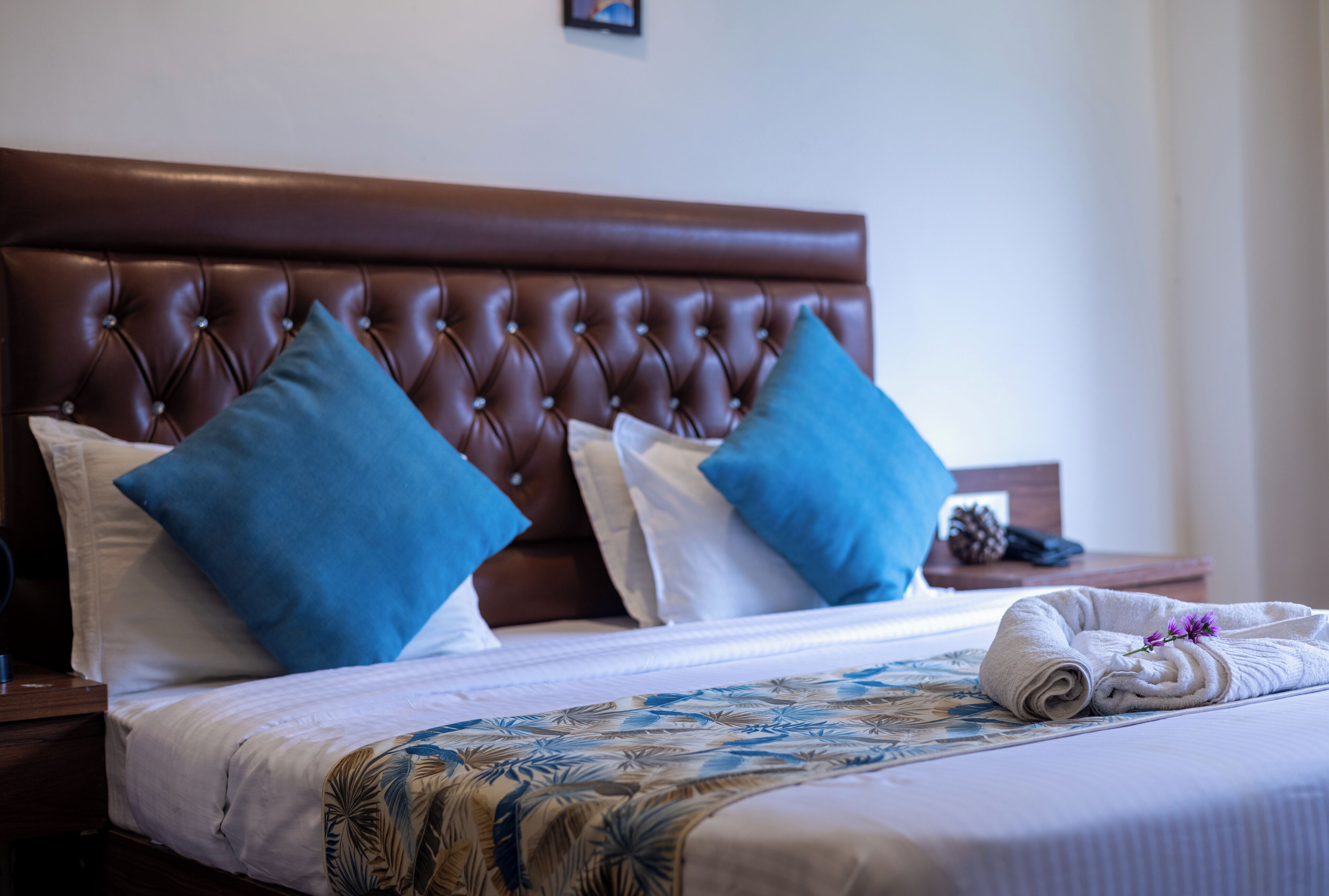 Un letto rifatto con una coperta a fiori, due cuscini blu e una testiera marrone.
