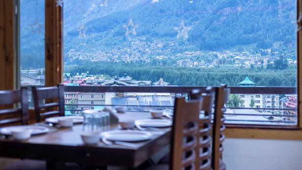 Ein Essbereich mit Tisch für zwei Personen, mit Blick auf eine Bergstadt mit Gebäuden und Grünflächen.