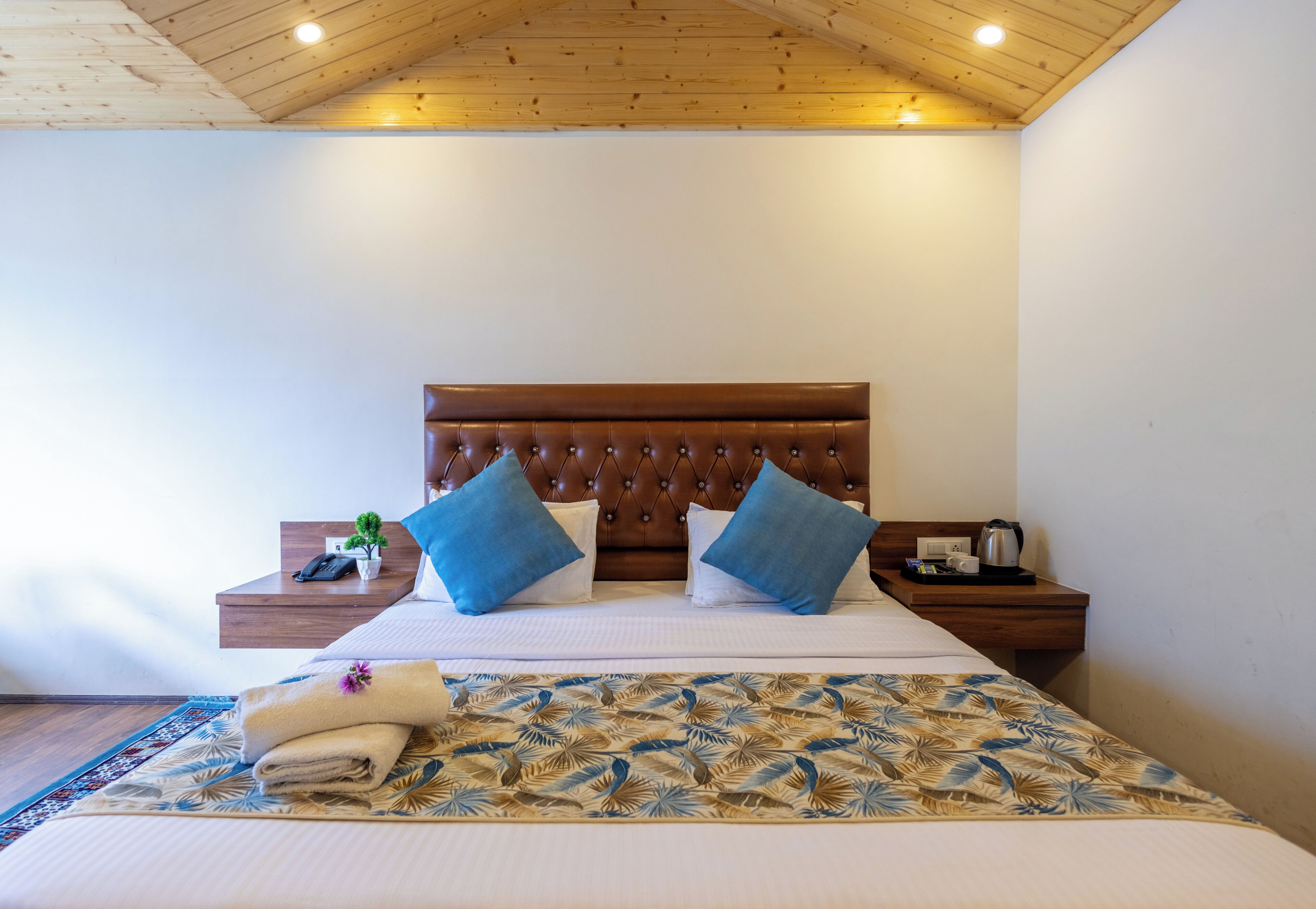 A neatly made bed with a patterned bedspread, a wooden headboard, and two blue pillows.