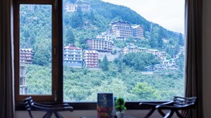 Ein Zimmer mit großem Fenster und Blick auf eine Hügellandschaft mit Gebäuden und Grünflächen.