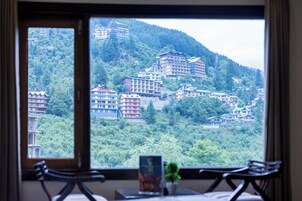 Quarto com uma grande janela que oferece vista para uma colina com edifícios e vegetação.