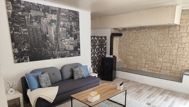 A modern living room with a gray sofa, a coffee table, and a cityscape painting on the wall. - 2-room apartment village center (Etaux)