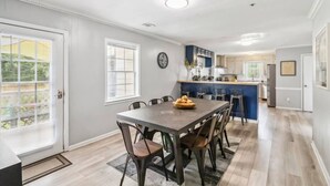 Una cocina moderna con una isla central, un comedor con una mesa y sillas de madera oscura, y vistas al exterior a través de amplios ventanales.