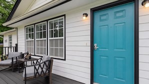 Una casa con puerta frontal color turquesa, un porche con dos sillas y un buzón.