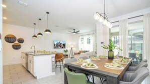 A modern kitchen with a central island, a dining area with a long table and chairs, and a living area with a sofa and a TV. - Stylish Home & Free Resort Access 2420 (Kissimmee)