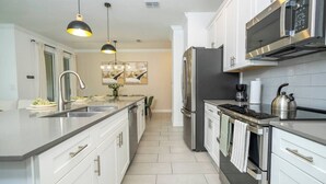 A modern kitchen with white cabinetry, stainless steel appliances, and pendant lighting. - Stylish Home & Free Resort Access 2420 (Kissimmee)