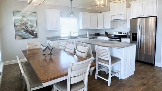 A spacious kitchen with white cabinetry, a central island, and a stainless steel refrigerator. - Bay Views at The Anchor Holds - formally Overboard (Grand Isle)
